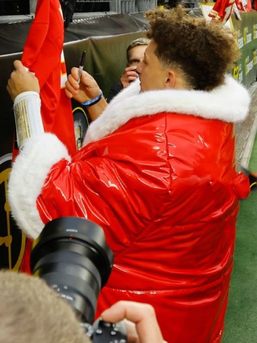 Person wearing a red puffer jacket with white fur trim, standing in front of a camera.