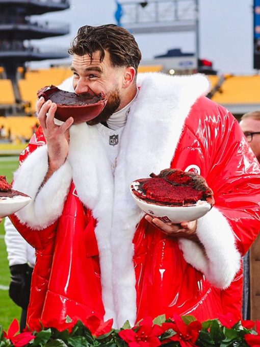 Person in a red coat with white fur trim holding a bowl of red food on a sports field.