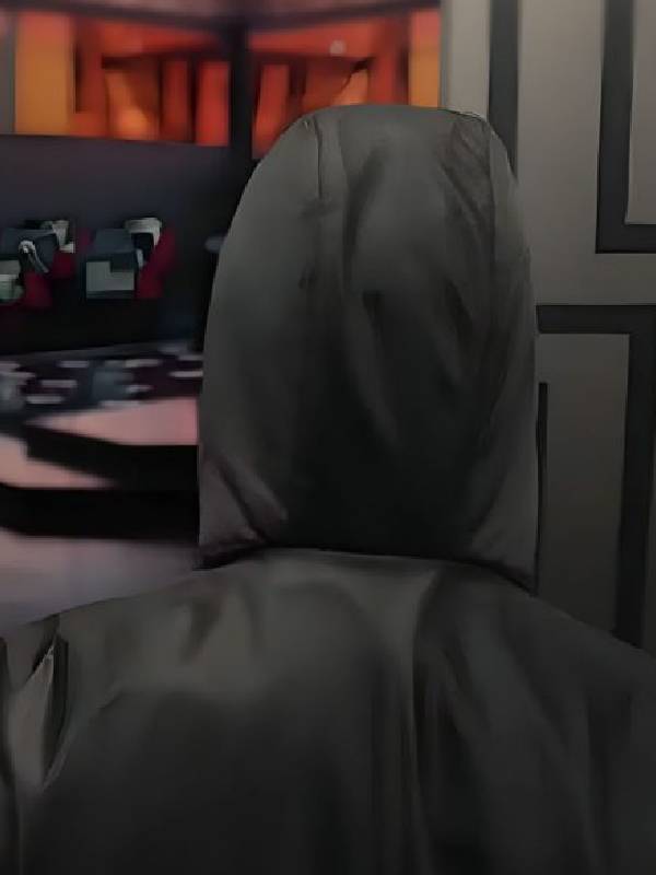 Person wearing a dark hooded jacket sitting in front of a computer screen with a colorful display.